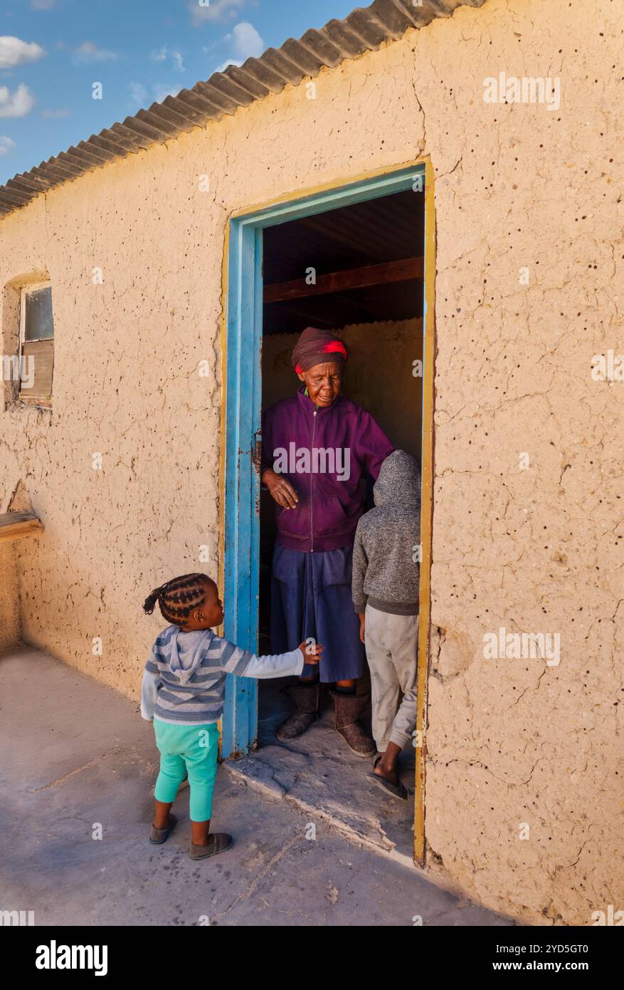 village african girl and her brother asking granny for help, entering the mud house, front door Stock Photo