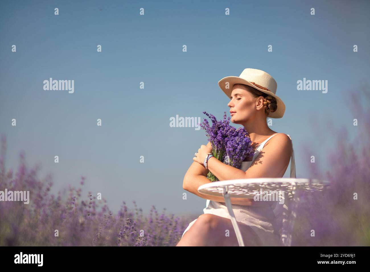 woman sitting in a field of lavender and wearing a straw hat. She is ...