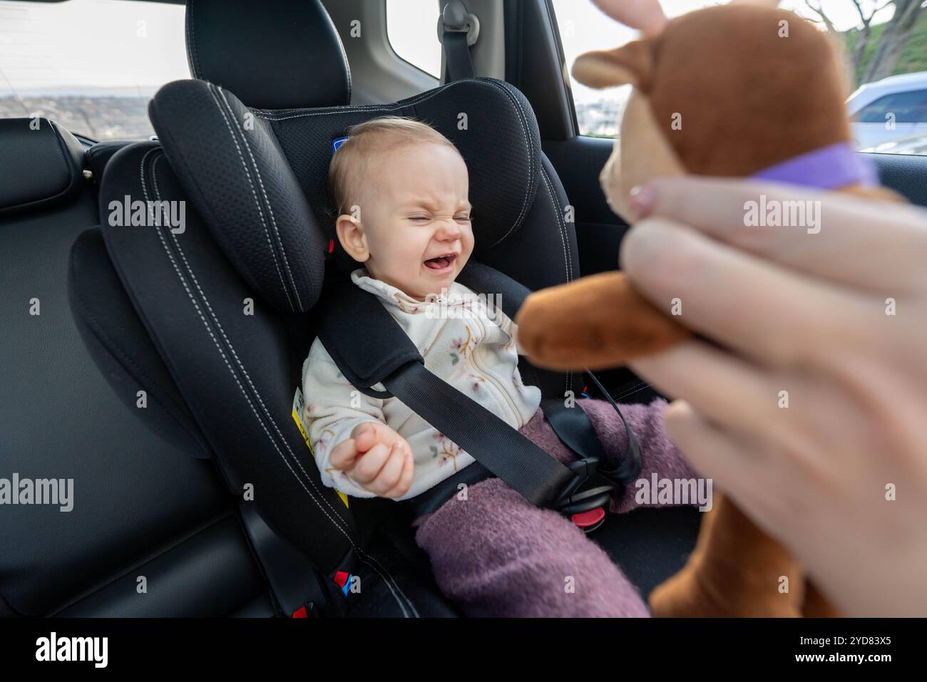 Mother trying to entertain baby in car seat with a toy. Concept of naughty toddler Stock Photo