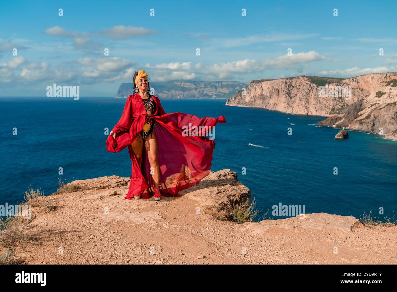 A woman in a red dress is standing on a rocky cliff overlooking the ...