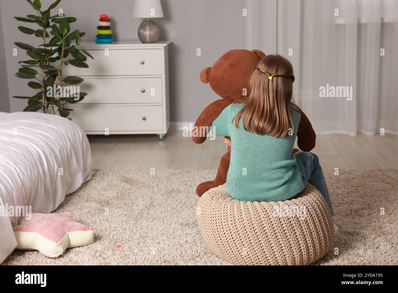 Autism concept. Lonely little girl with teddy bear on pouf at home ...