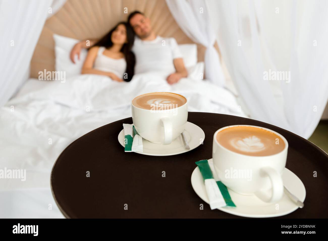 Room service delivering 2 cups of coffee to a hotel room for married couple lying in a bed in the morning Stock Photo