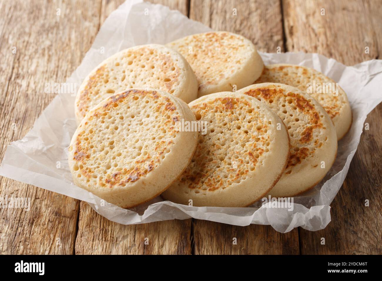 Porous Homemade English Crumpets close-up on parchment paper on old table. Horizontal Stock Photo