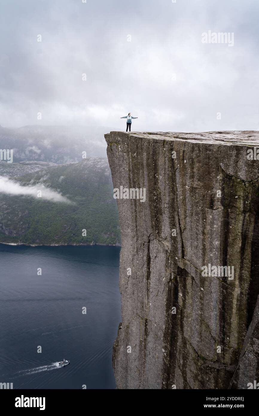 A woman with her arms outstretched on the edge of the Preikestolen ...