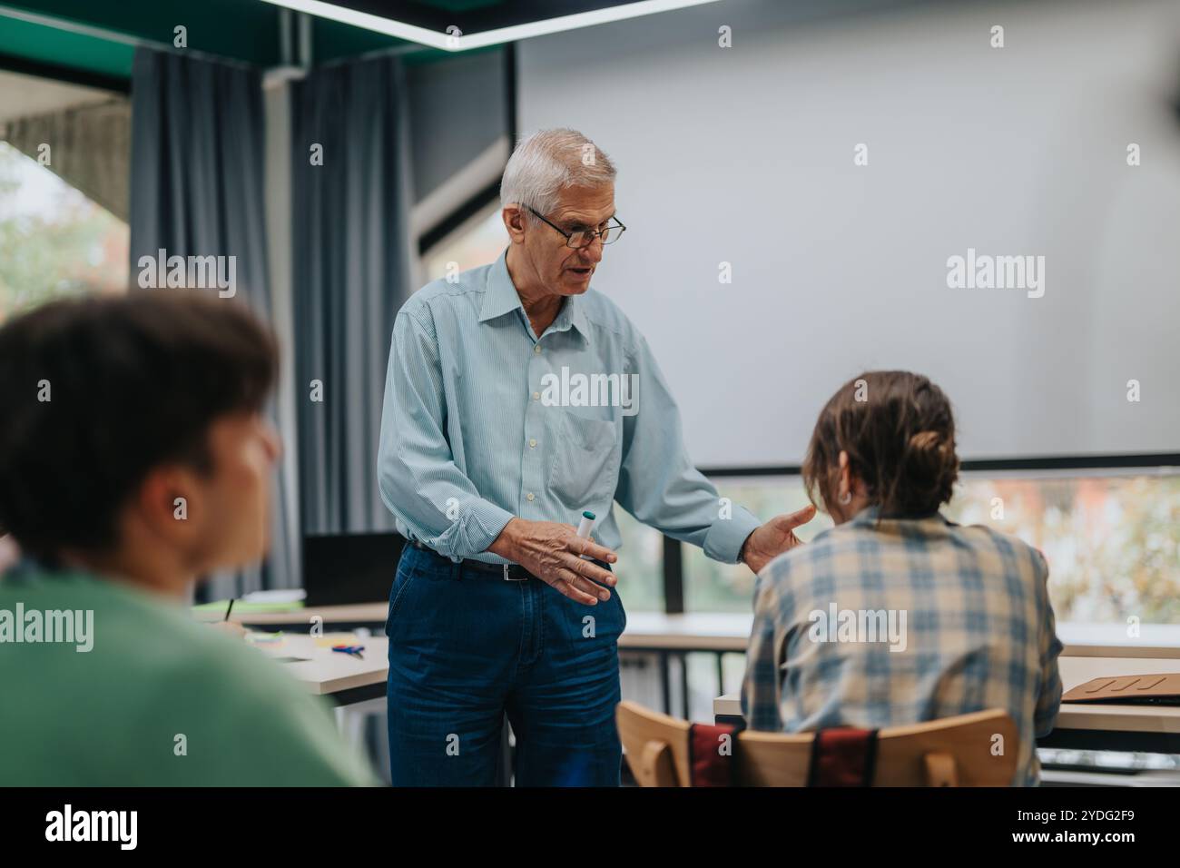 Elderly professor engaging with attentive students in classroom setting Stock Photo