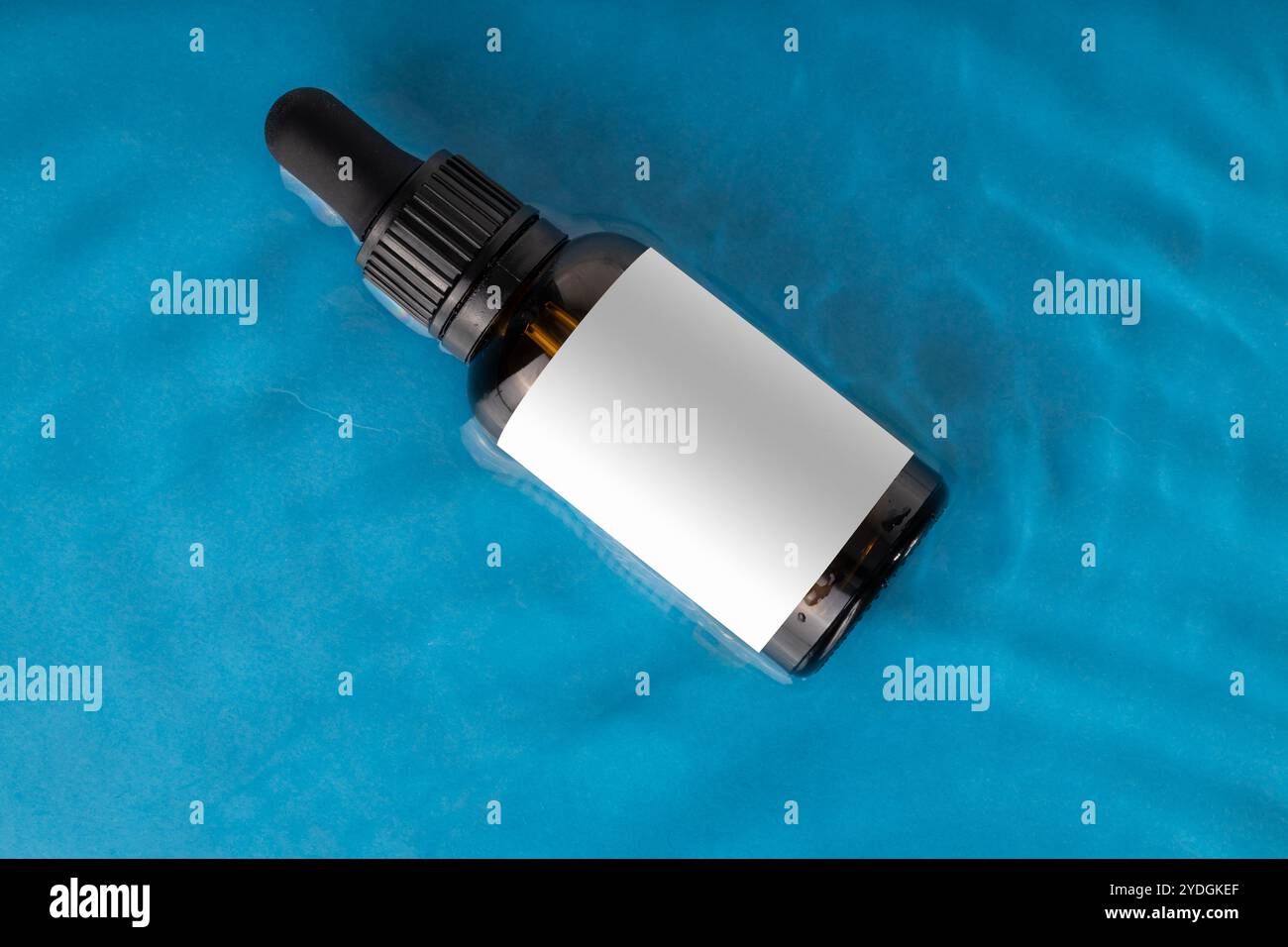 Amber Dropper Bottle on Blue Water Surface with Blank Label Stock Photo