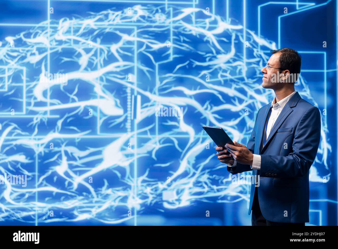 Data scientist analyzes AI brain models on tablet with large digital brain displayed behind. IT expert using machine learning to better understand and develop artificial intelligence Stock Photo