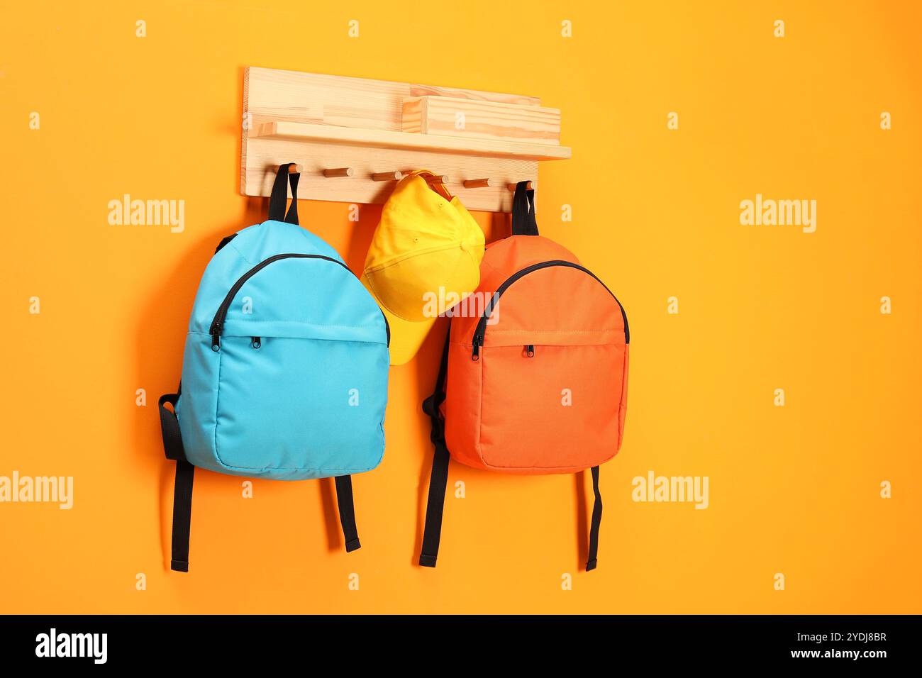 Bright backpacks and cap hanging on orange wall Stock Photo
