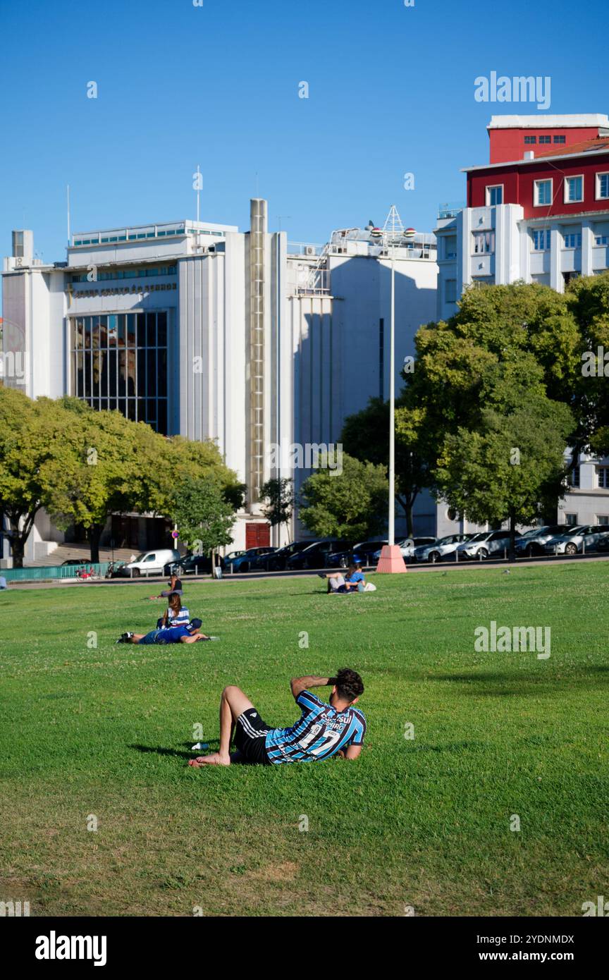 Relaxed afternoon in Alameda Park, Lisbon, with people lounging on the grass against a backdrop of historic and modern architecture Stock Photo
