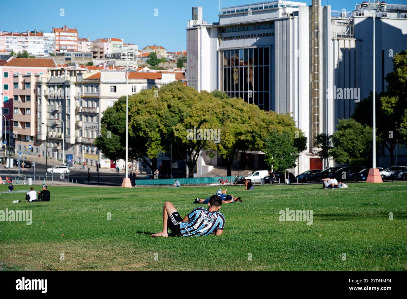 Relaxed afternoon in Alameda Park, Lisbon, with people lounging on the grass against a backdrop of historic and modern architecture Stock Photo