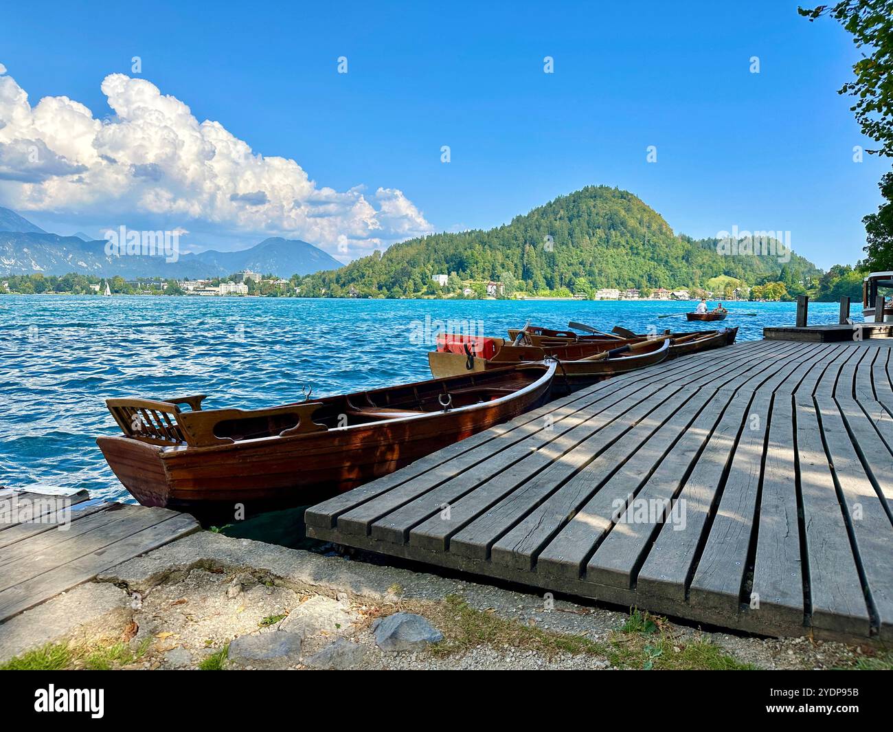 The photo beautifully captures a boat gently floating on a serene lake, surrounded by a stunning mountain landscape in Slovenia on a warm summer day. - Smartphone Captured Stock Image