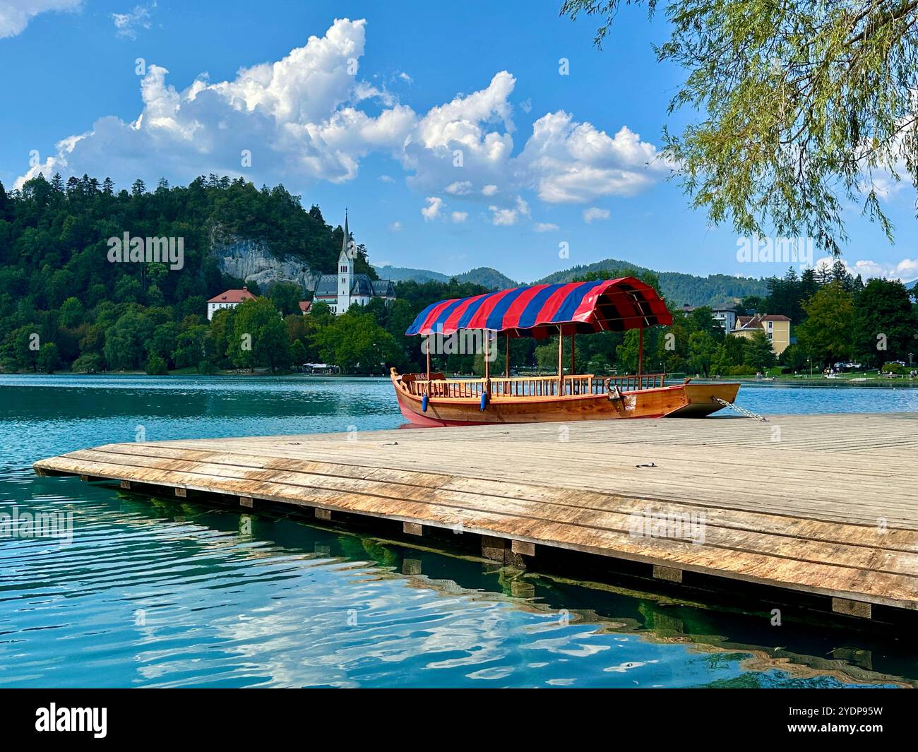 The photo beautifully captures a boat gently floating on a serene lake, surrounded by a stunning mountain landscape in Slovenia on a warm summer day. - Smartphone Captured Stock Image