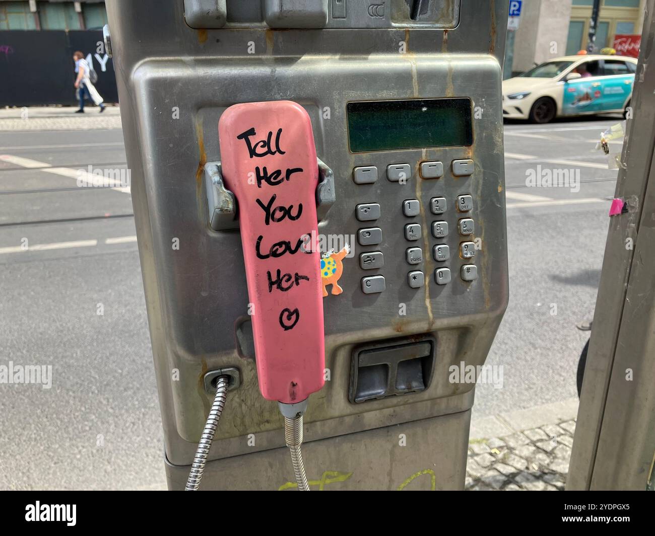 A payphone with the message 'Tell Her You Love Her' written on the pink receiver near Alexanderplatz Bahnhof. Mitte, Berlin, Germany. 22nd May 2023. - Smartphone Captured Stock Image