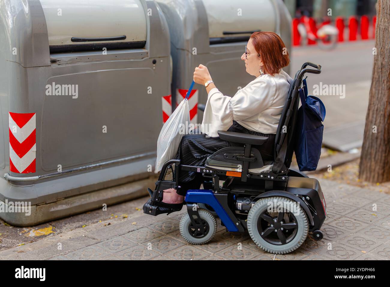 Woman in Wheelchair Using Public Trash Bin for Recycling Stock Photo