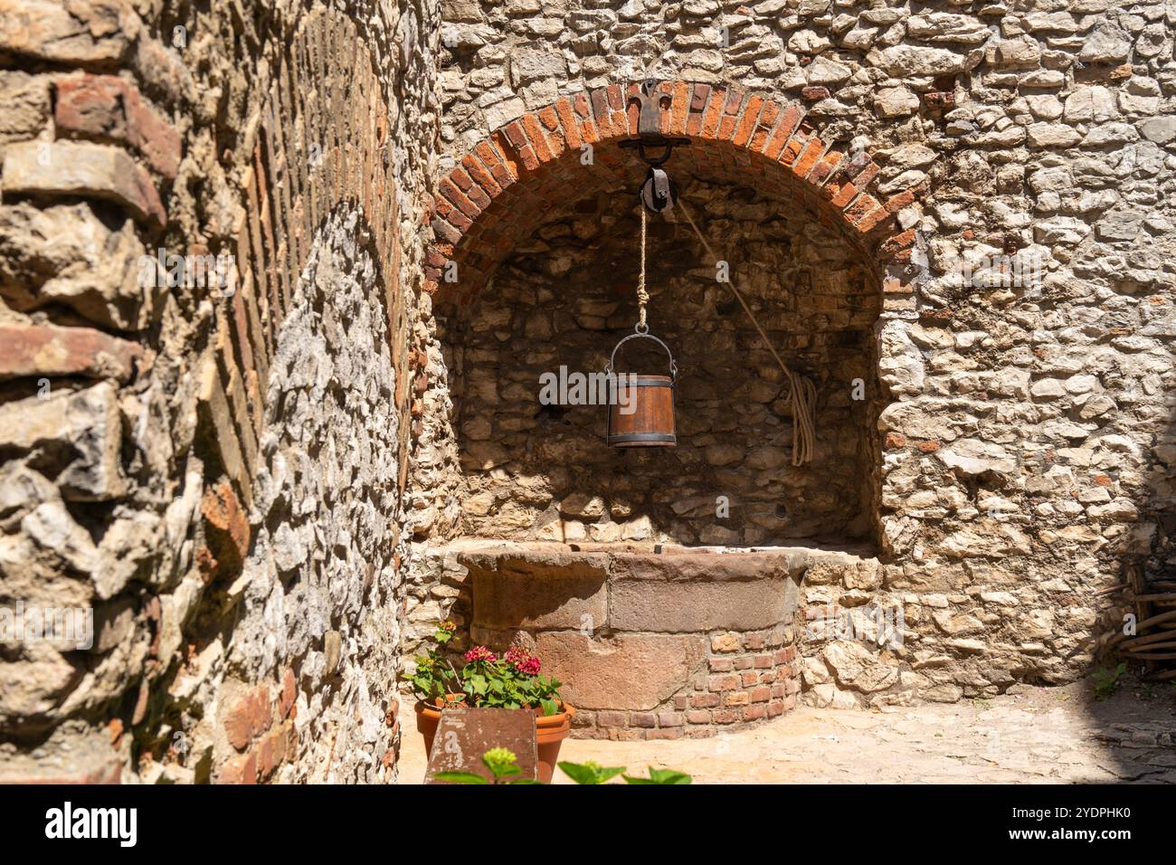 Old stone well with wooden bucket in front of a stone wall Stock Photo