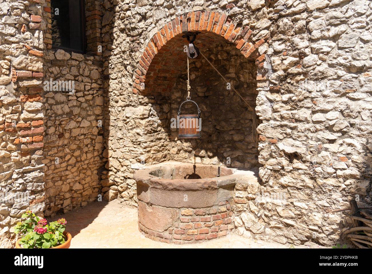 Old stone well with wooden bucket in front of a stone wall Stock Photo