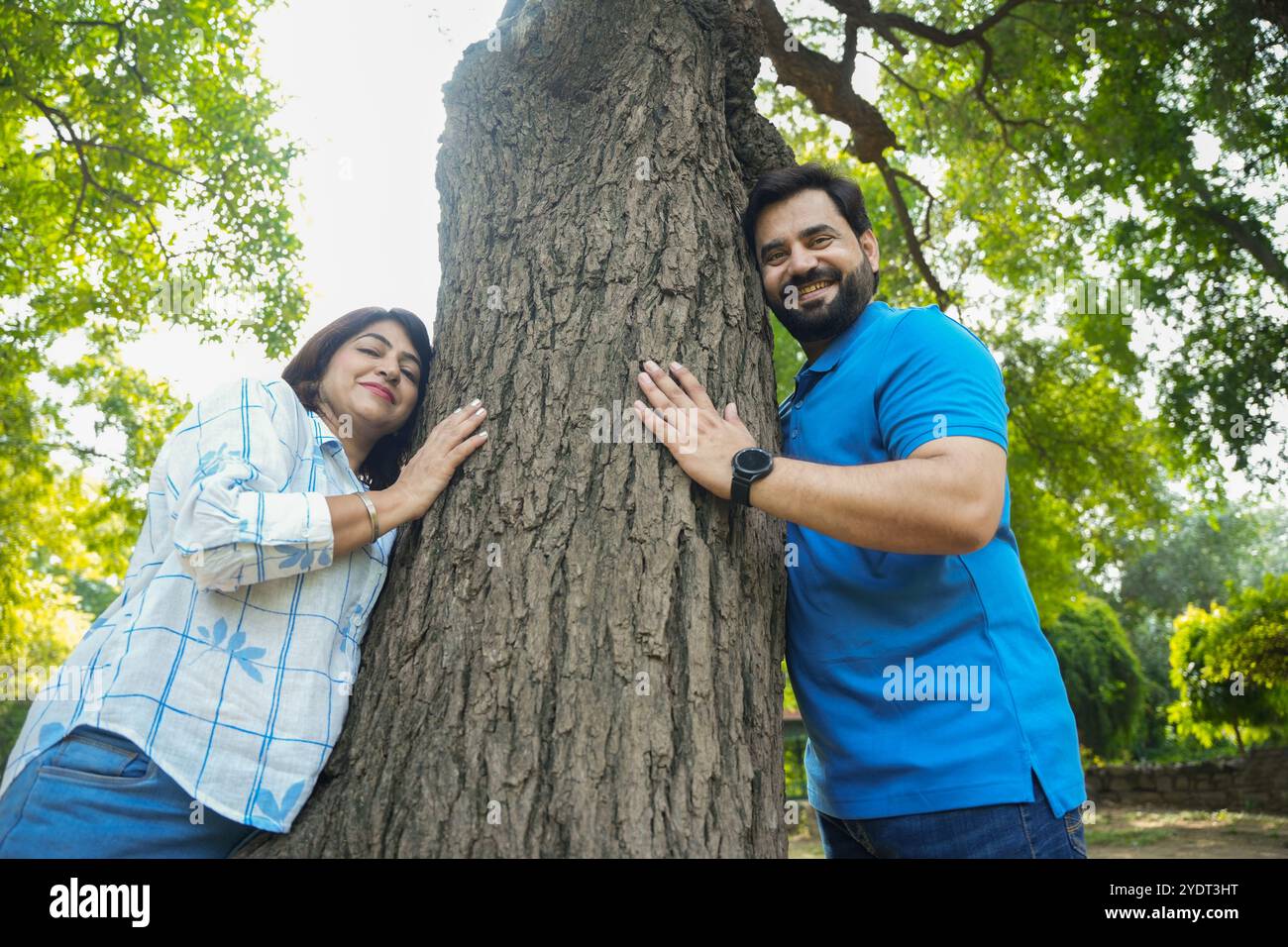 young happy indian couple in forest hugs large tree, Save environment ...