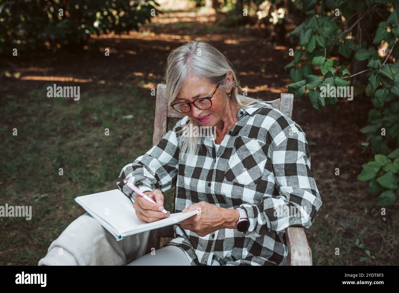 Beautiful older women is sitting in the garden and writing in her diary