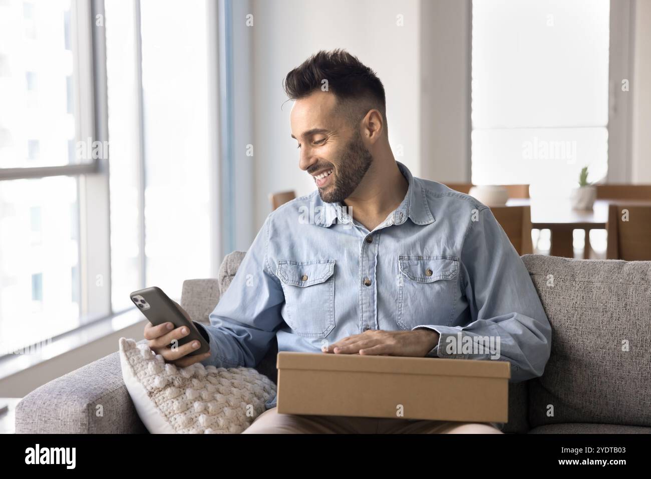 Happy young Hispanic customer guy holding smartphone and logistic box Stock Photo