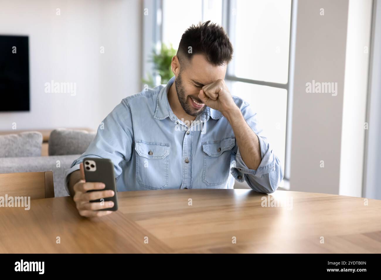 Cheerful young Latin man using mobile phone and laughing Stock Photo