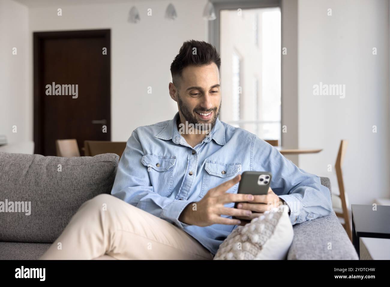 Cheerful young Latin man typing on mobile phone Stock Photo