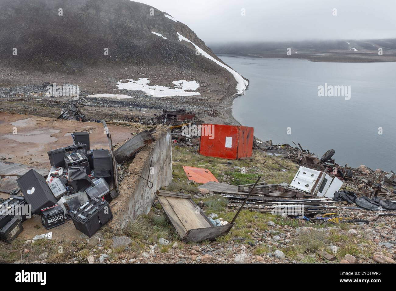 Old batteries, junkyard in rocky coastal landscape with snow remains, arctic settlement Ittoqqortoormiit, Scoresbysund or Scoresby Sund or Greenlandic Stock Photo