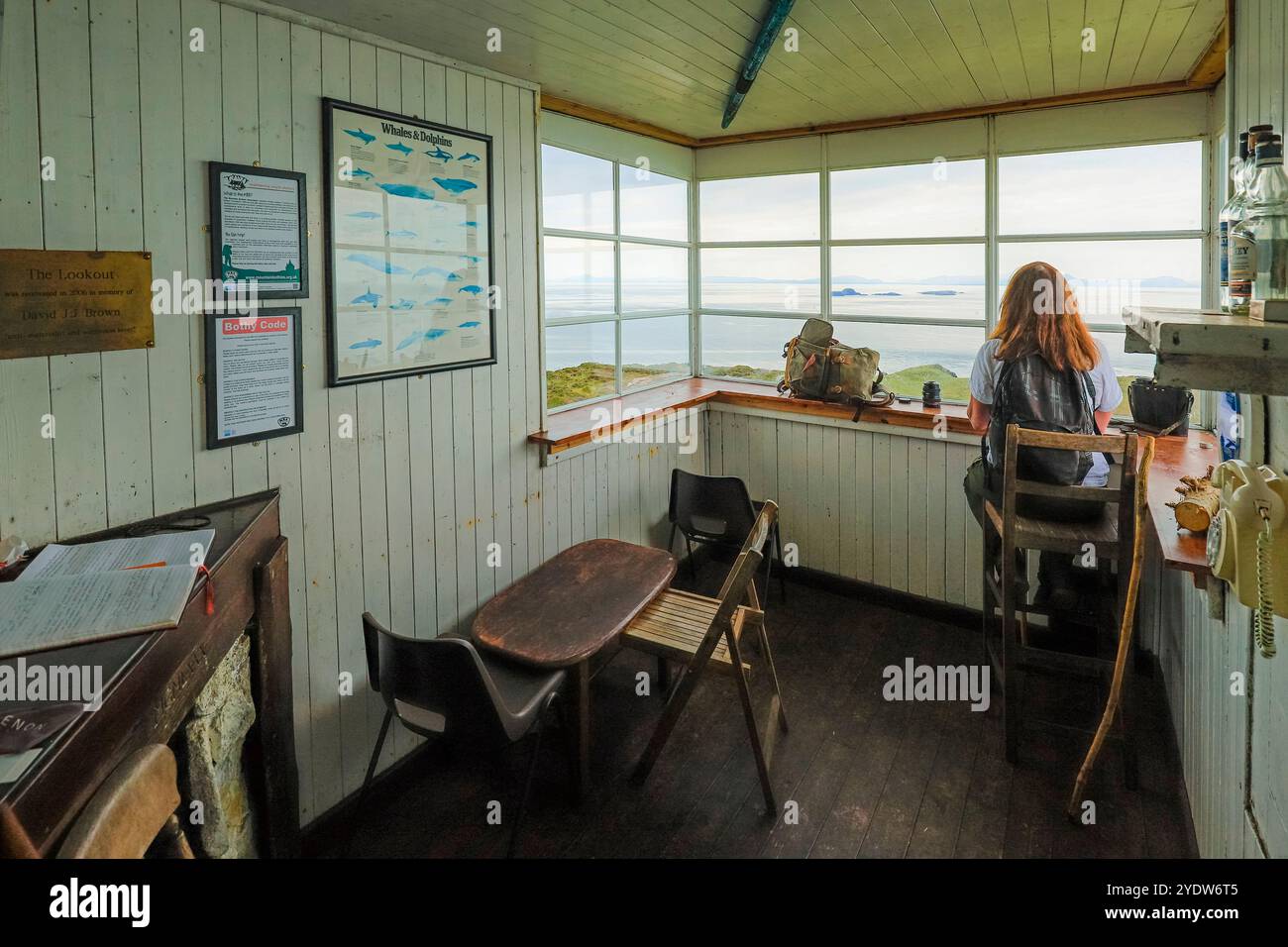 Woman hiker looks out from Rubha Hunish Coast Guard lookout bothy to the Shiant Isles and Harris, Rubha Hunish, Duntulm, Skye, Scotland Stock Photo