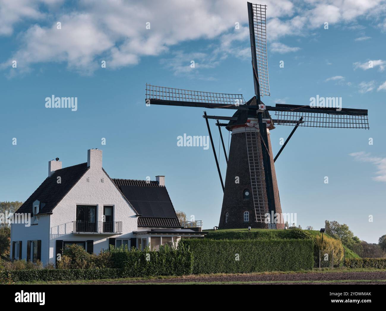 Korenmolen De Roosdock in NuenenA scenic view of the historic windmill de Roosdonck in Nuenen, Noord-Brabant, with modern house, blue sky, and green l Stock Photo