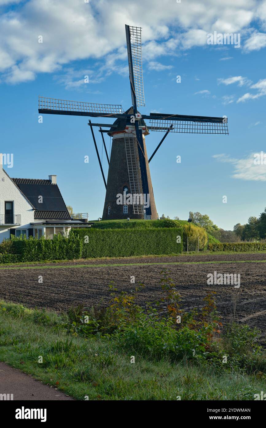 Korenmolen De Roosdock in NuenenA scenic view of the historic windmill de Roosdonck in Nuenen, Noord-Brabant, with modern house, blue sky, and green l Stock Photo