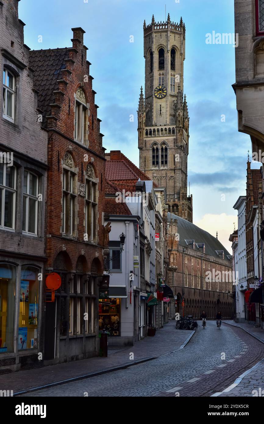 Belfry of Bruges, medieval brick buildings and two cyclists just after sunrise on the empty Wollestraat, Bruges, Belgium Stock Photo