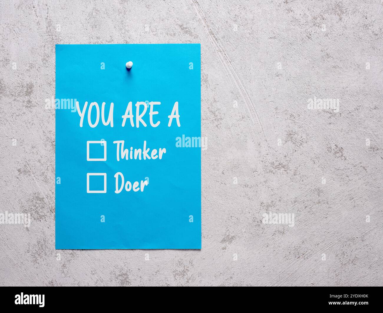 You are a thinker or doer checkboxes on a blue sheet of paper pinned to a white concrete wall. Stock Photo