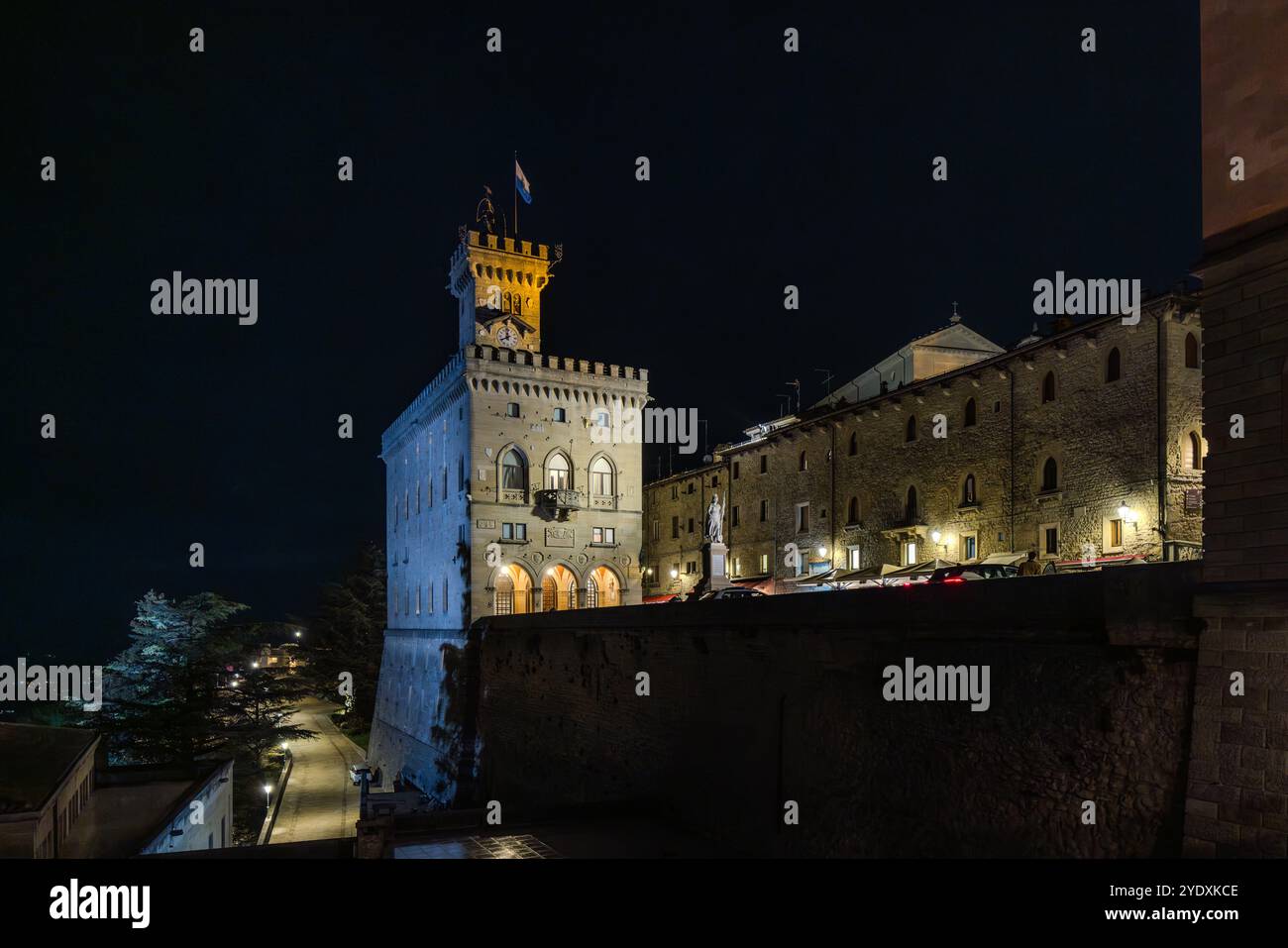 The Piazza del Comune in San Marino at night. The historic town hall (Palazzo Pubblico) with its striking bell tower can be seen in the foreground.  The surrounding stone buildings are illuminated and give the scene a special atmosphere. The night gives the city a calm and picturesque character. Piazza della Libertà, Città di San Marino, San Marino Stock Photo