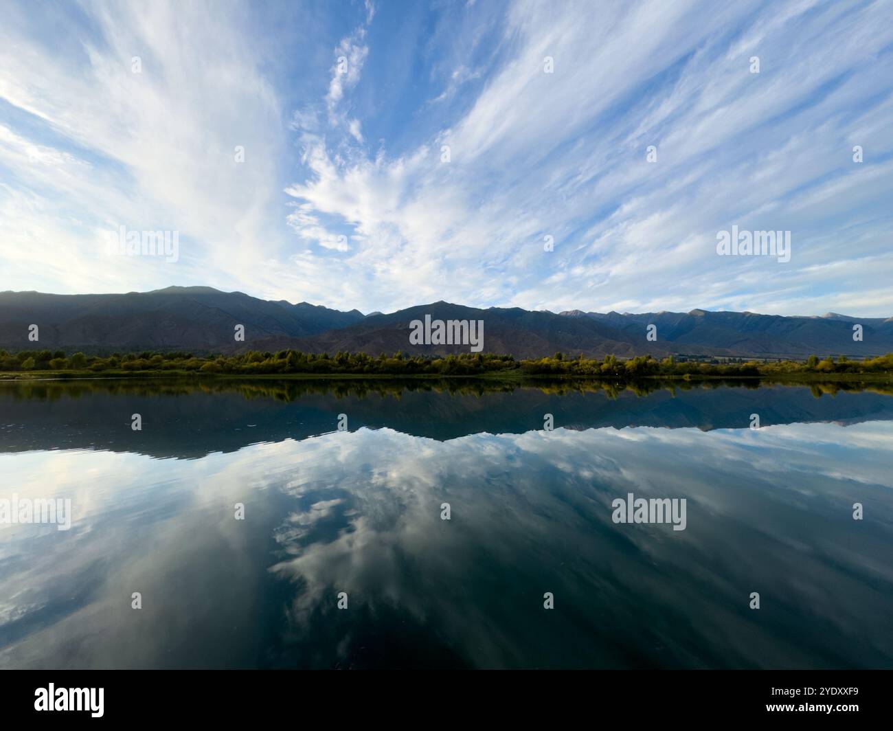 The calm water of a mountain lake reflects the blue sky and white ...