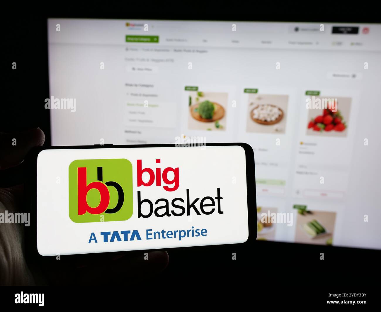 Person holding smartphone with logo of Indian online grocery company BigBasket on screen in front of website. Focus on phone display. Stock Photo