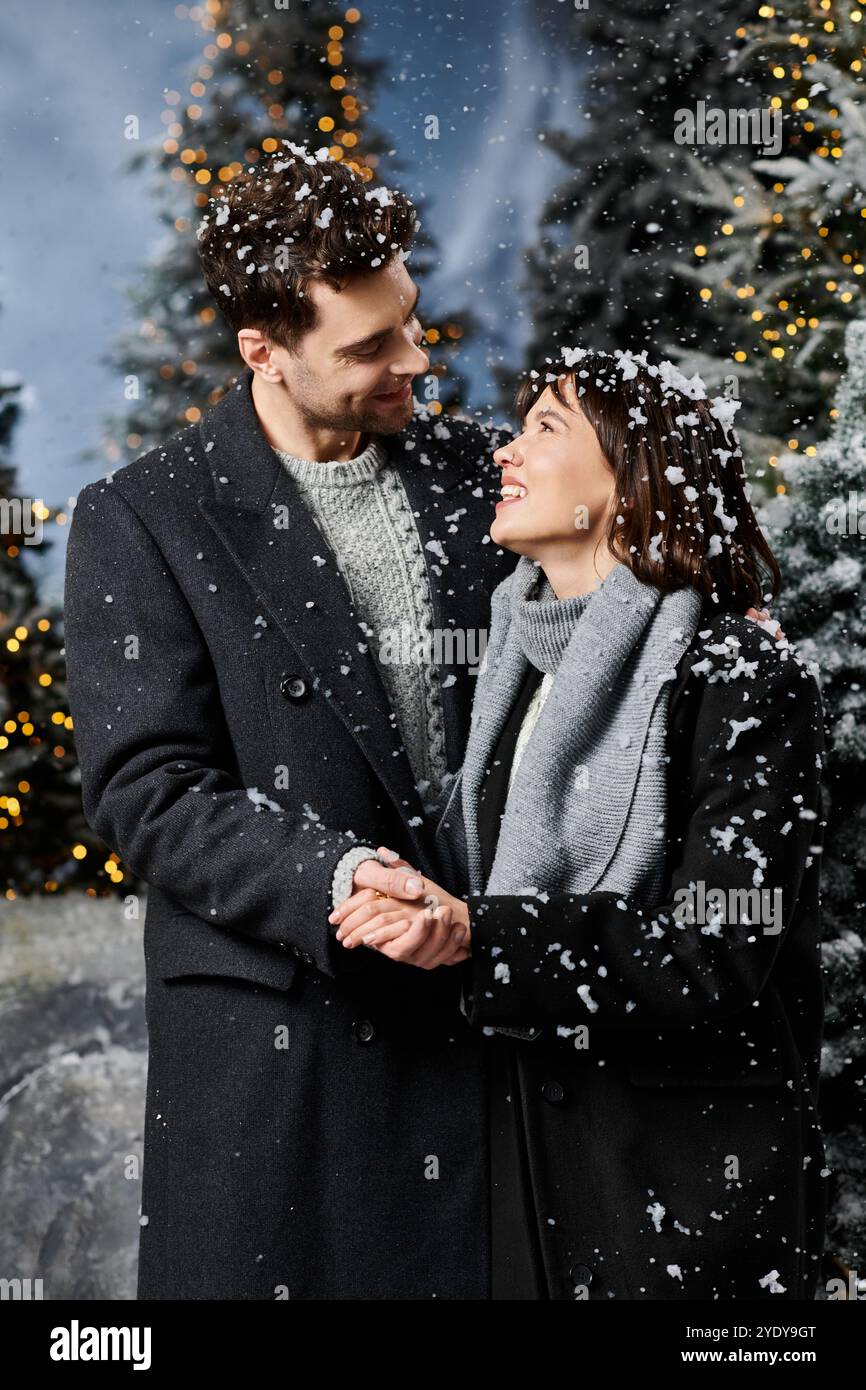 A joyful couple in winter coats shares a tender moment amidst snowy ...