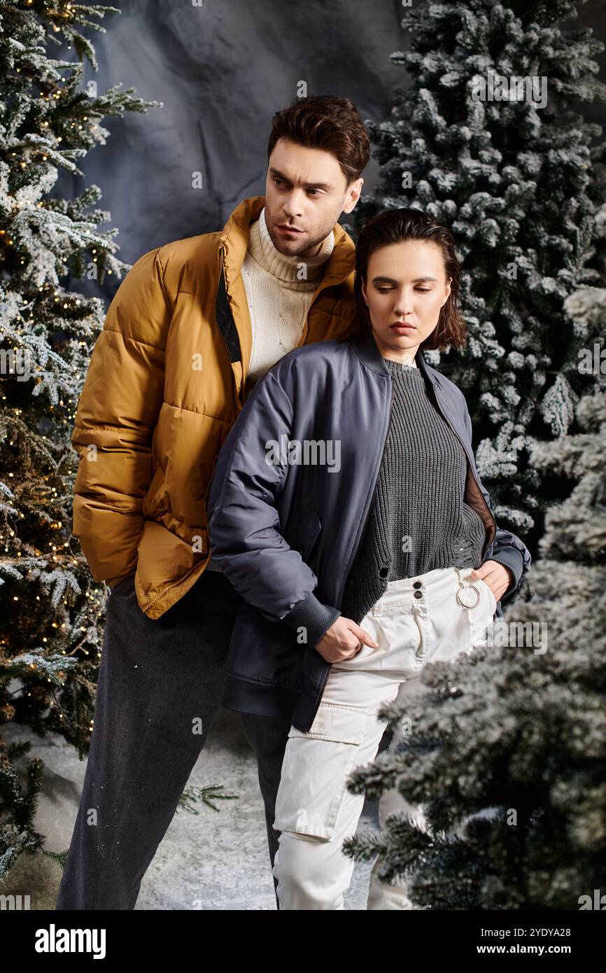 A warm-hearted couple embraces the festive spirit, surrounded by snow-laden pine trees on a winter day. Stock Photo