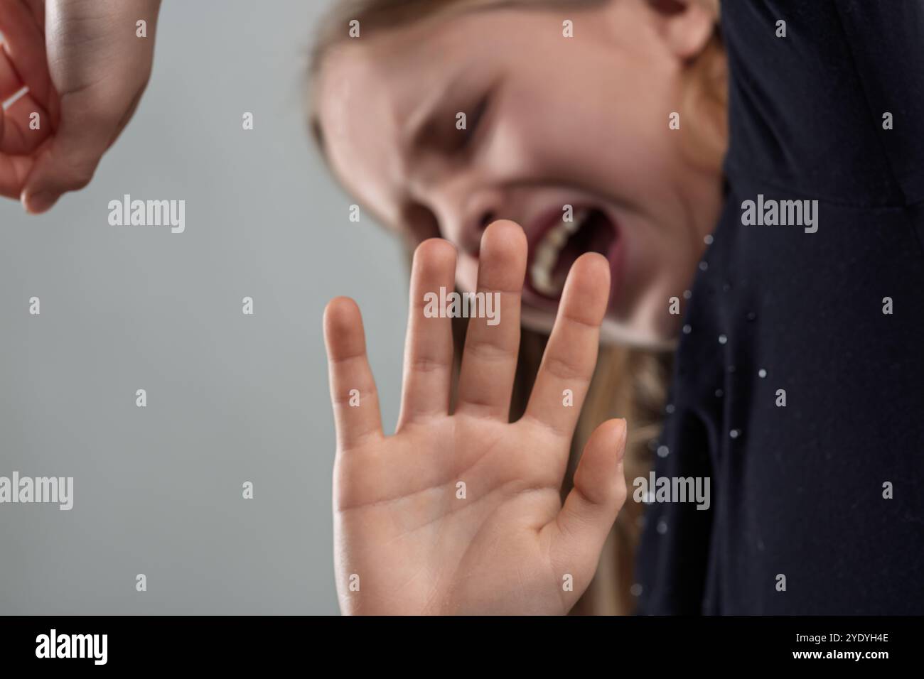 Young girl screaming with her eyes closed while raising her hand in a defensive gesture, expressing fear, anxiety, and the need for protection against Stock Photo