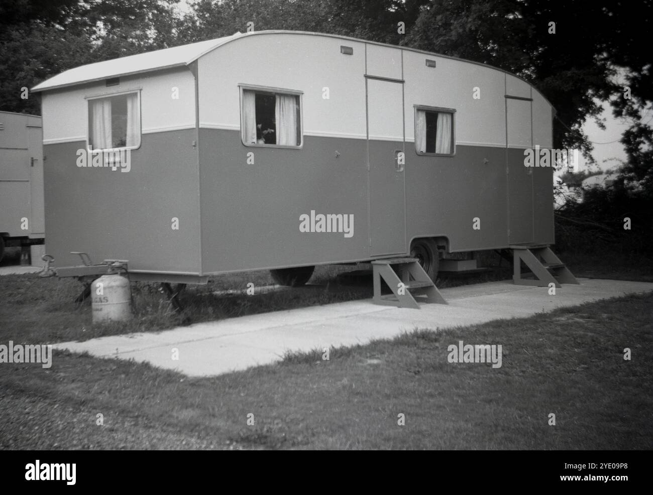 1950s, historical, a static holiday caravan of the era, parked on a concrete floor in a field, wooden steps up to two side entrance doors, England, UK. The rise in the number of people who owned motor cars in the 1950s and 60s meant that families could now travel to and make use of such holiday caravans, either rented for a week or owned, on a much more frequent basis than before. Advertising promoted them as a being a 'homobile', literally, a house on wheels. Stock Photo