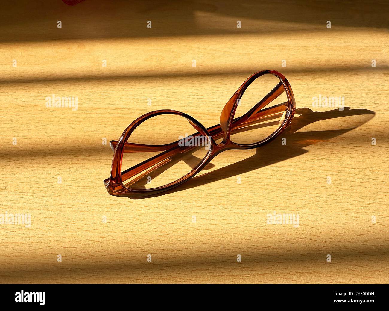 Pair of brown glasses with brown frames on a desk with sunlight sining through a window with blinds. Work from home concept. - Smartphone Captured Stock Image