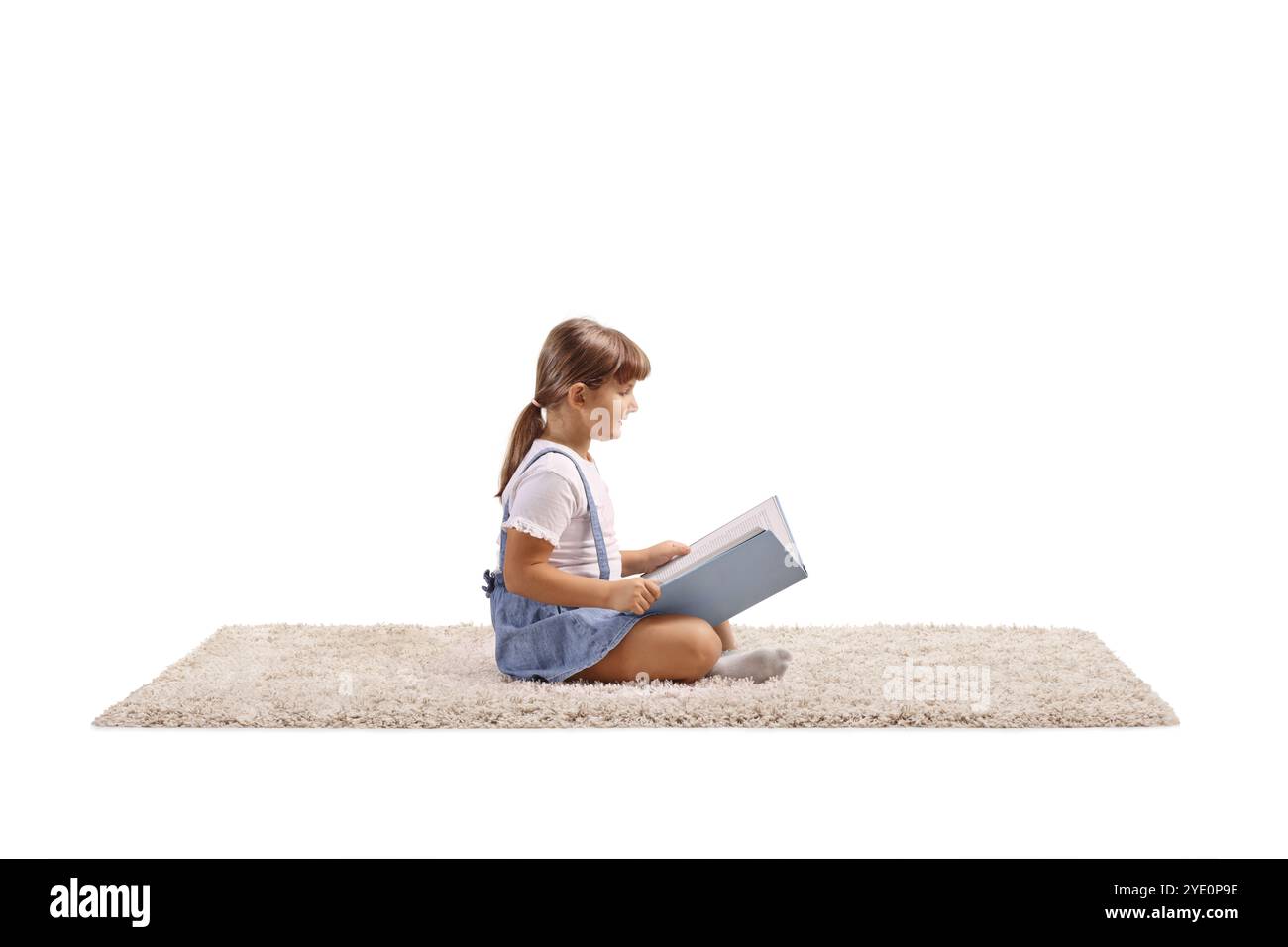 Little girl sitting on a carpet and reading a book Stock Photo - Alamy
