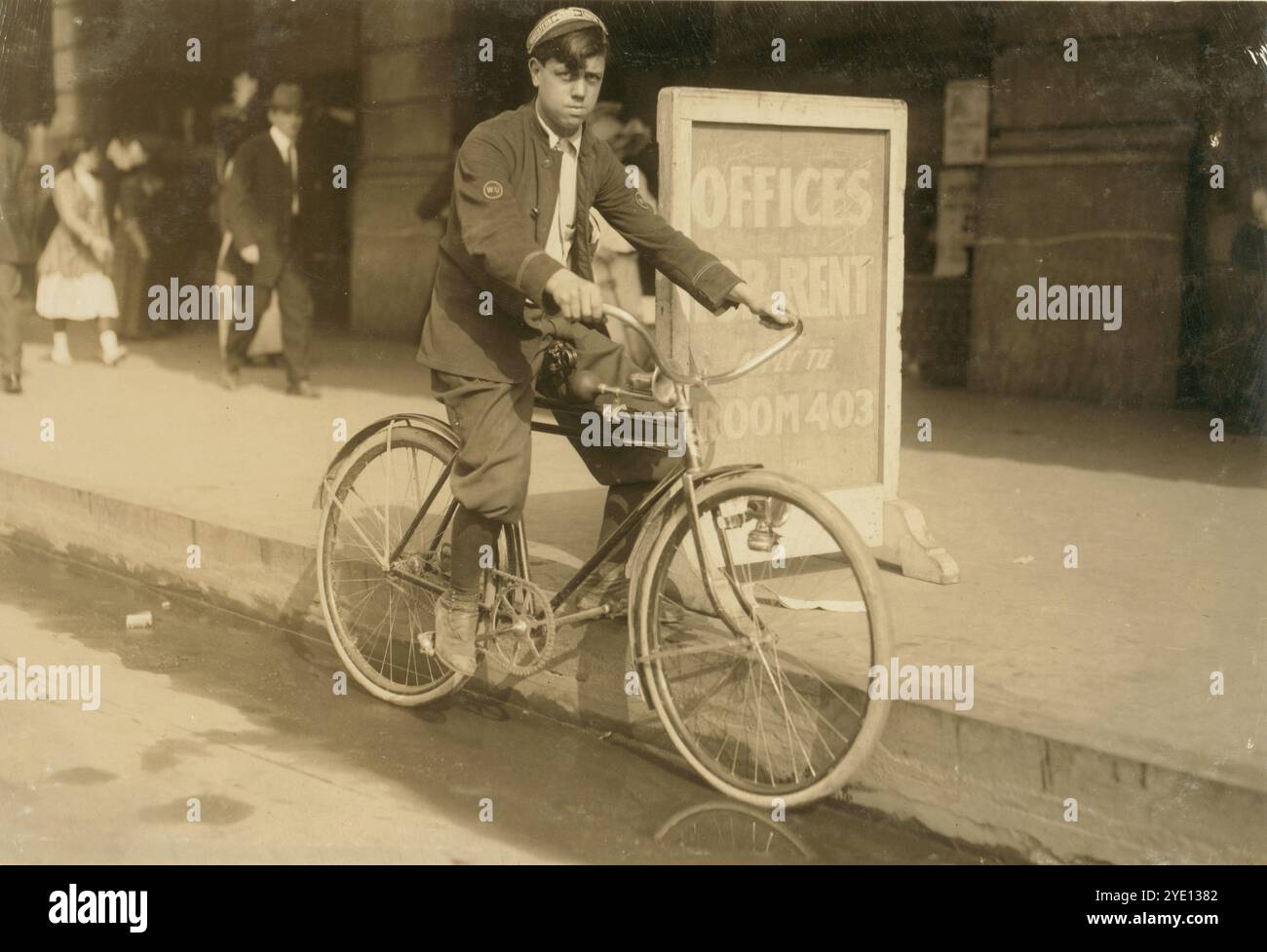 New Orleans, 1913. "A typical messenger boy in New Orleans. The telegraph companies are trying to obey the law, and few violations occur." Messenger boy on bicycle, posed by cement sidewalk. In background is sign "Offices For Rent", pedestrians on urban sidewalk. Messenger has "W.U." badges on his clothes, identifying as working for Western Union.   Photo Credit: Lewis Wicke Hine.   Vintage American Photography 1910s. Child Labour Project.  Credit: Lewis Hines Stock Photo