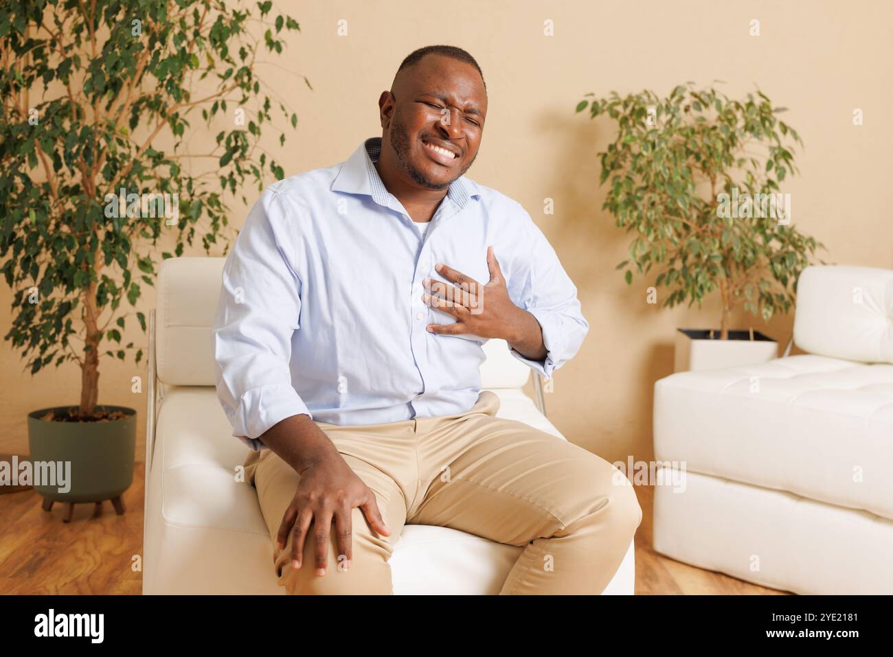 An African American man clutches his chest in pain, possibly having a heart attack or cardiac arrest. The image shows clear signs of distress and an u Stock Photo