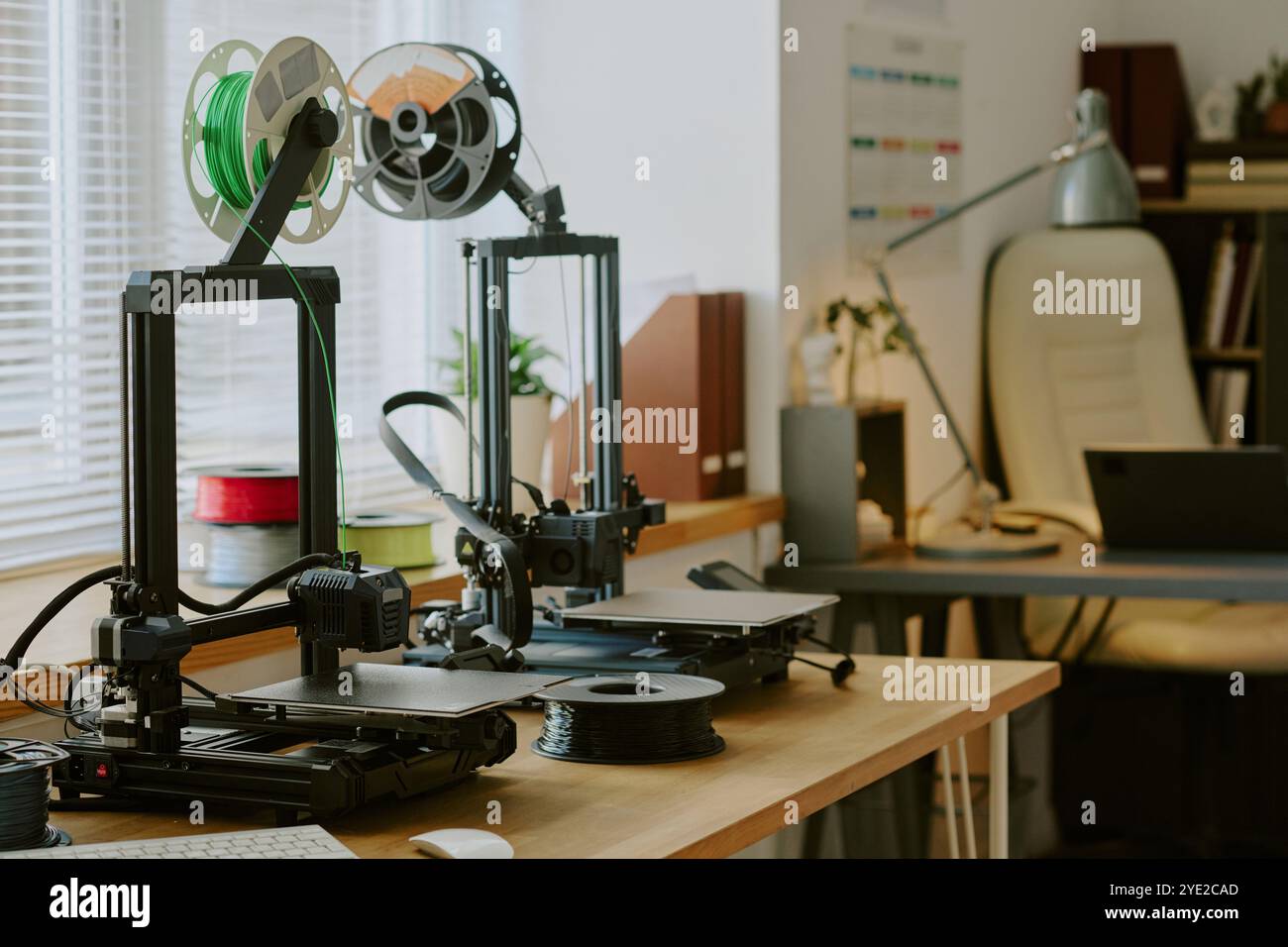 Featuring two printers with green and black spools printing on a wooden desk in a well-organized office space with various gadgets and equipment visible Stock Photo