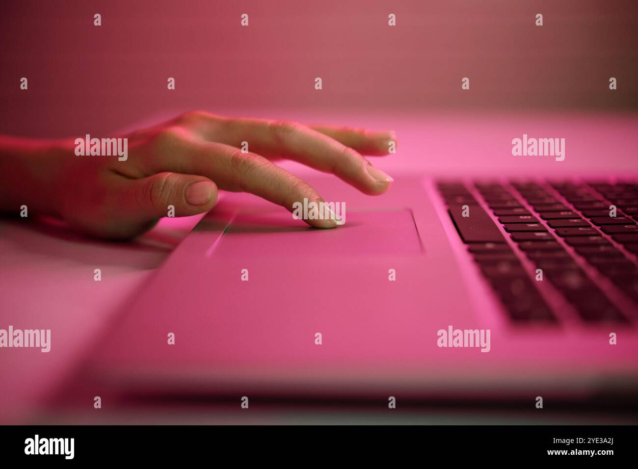 Hand hovering over laptop trackpad under pink ambient lighting ...
