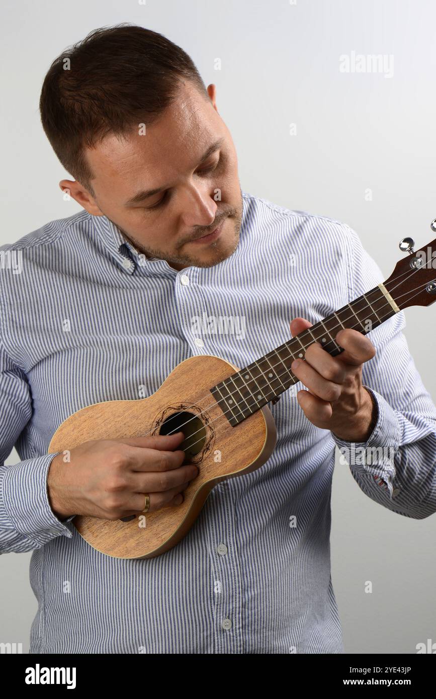 Young caucasian man playing ukulele hobby leasure grey background Stock Photo