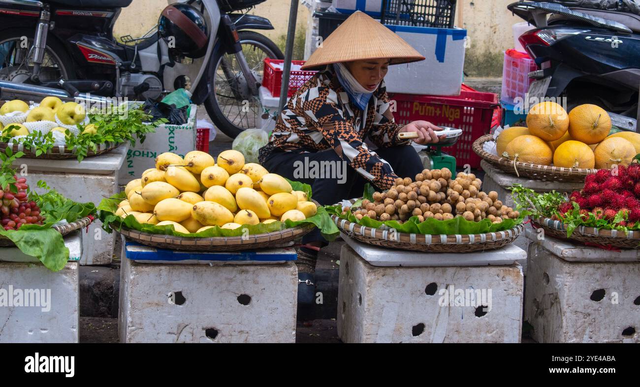 Hanoi, Vietnam: Vietnamese woman wearing traditional conical hat Non La and selling fruits at Dong Xuan Market, built by the Frenchs in 1889 Stock Photo