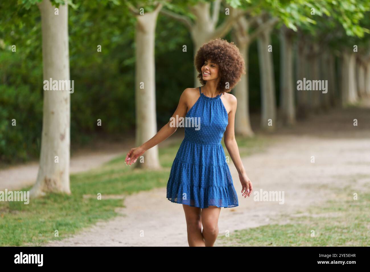 A woman in a blue dress is walking down a path in a park. She is ...