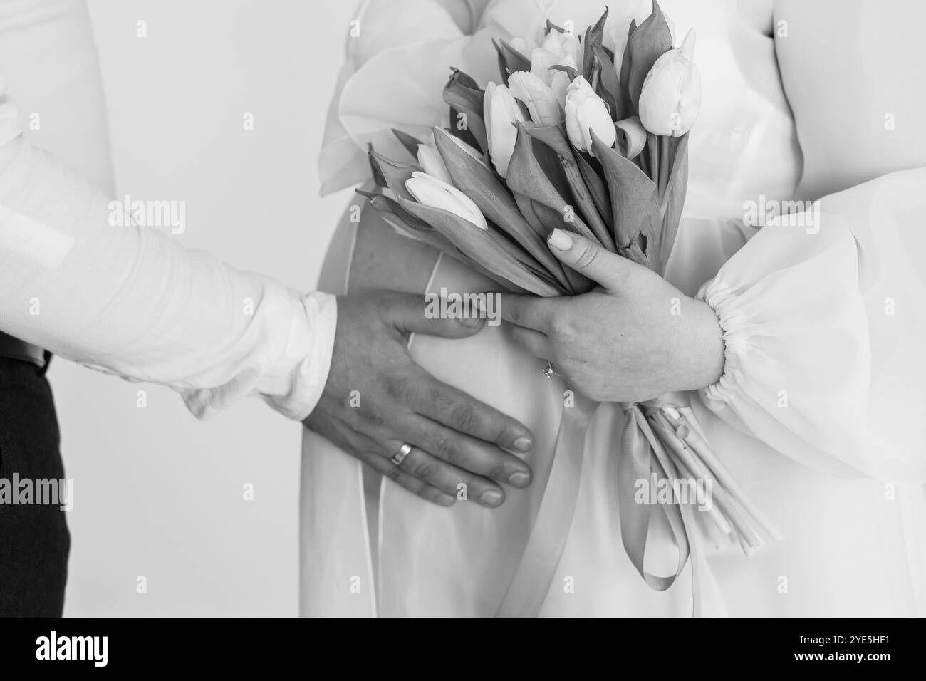 Intimate Anticipation: A Couple's Touch During Pregnancy with Tulips. Stock Photo