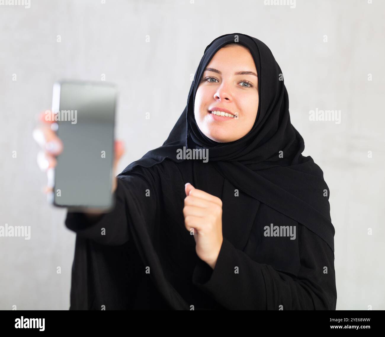 smiling Muslim woman in traditional black hijab shows blank smartphone ...