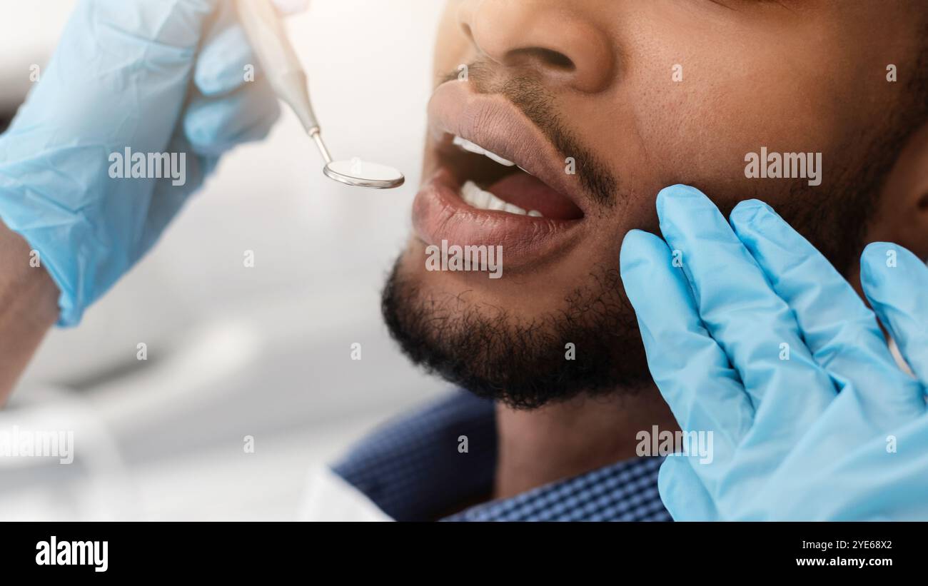 Dentist hands in gloves checking black man mouth Stock Photo